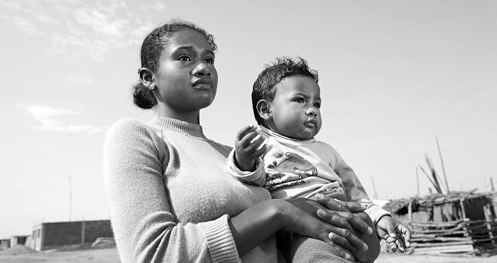 Retrato en primer plano de una joven madre afroperuana que sostiene a su bebé en brazos, ambos mirando al frente.