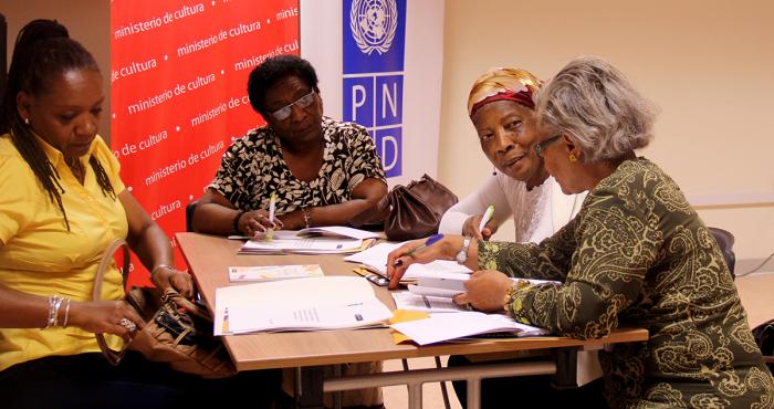 En la imagen se ve a cuatro mujeres afroperuanas adultas que trabajan sentadas a una mesa.