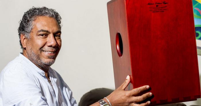 En la imagen aparece Rafael Santa Cruz, quien mira hacia la cámara mientras sostiene sonriente un cajón peruano.